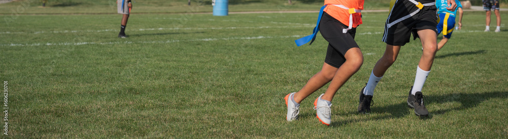 Children participate in a flag football practice on a sunny day at a local park with green grass and ample space for play Children participate in a flag football practice on a sunny day at a local park with green grass and ample space for play