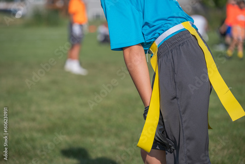 Children participate in flag football practice at a community park in summer under clear skies