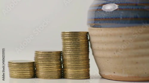 Stacks of coins form a rising graph next to a ceramic pot
