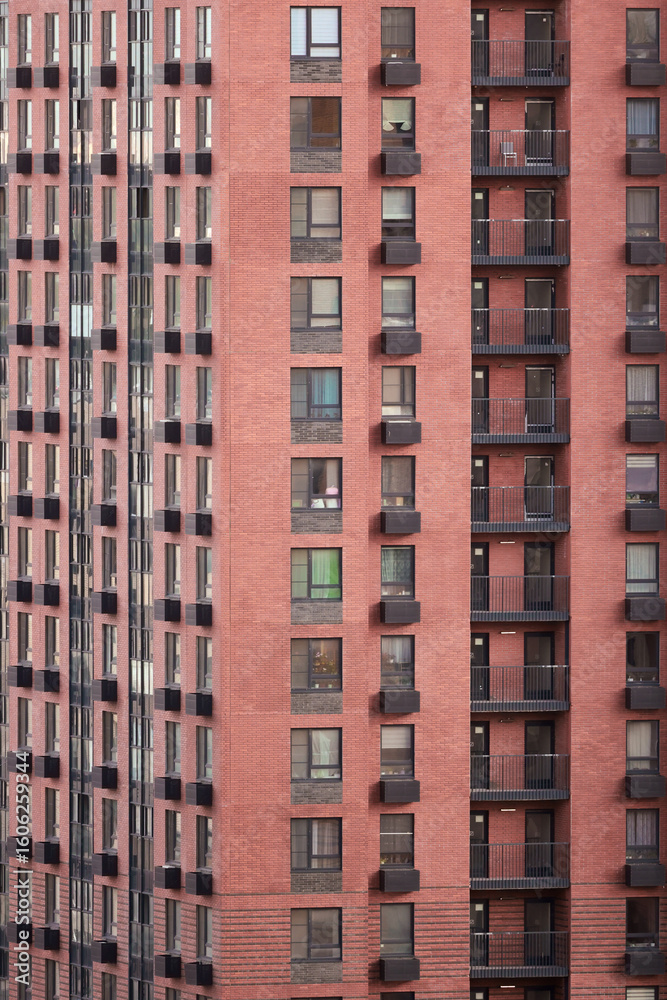 Fototapeta premium Facade Of A Modern Multi-Storey Residential Building With Red Brick Walls, Windows And Balconies. Urban Architecture Pattern And Texture. Vertical Shot.