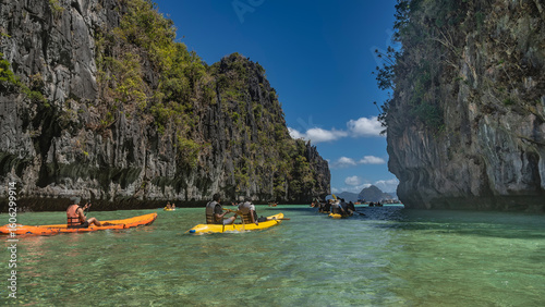 Tourist canoes sail through a beautiful turquoise lagoon surrounded by sheer cliffs. Tropical vegetation on the slopes. Blue sky, clouds. Philippines. Palawan. Big Lagoon. Bacuit archipelago. 