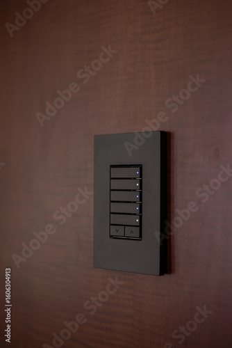 Close-up of a modern black smart home light switch keypad with LED indicators, installed on a rich dark wood wall panel for home automation.