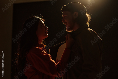 Young adult Hispanic woman and young adult Caucasian man rehearsing dramatic scene together during acting audition, standing close and making intense eye contact on stage
