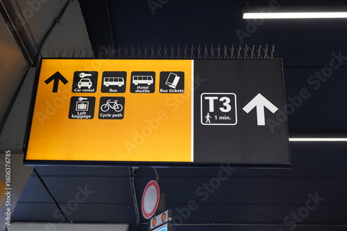 Photography Yellow directional sign at Fiumicino Airport, Rome, Italy, showing arrows for car rental, bus, hotel shuttle, ticketing, luggage services, and Terminal 3 walkway