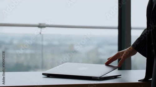 Business woman's hand gently touches the laptop cover, ready to shut down and leave