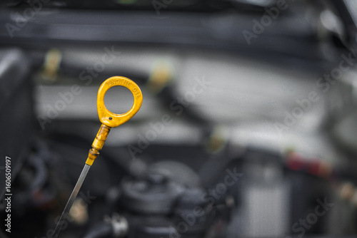Close up of yellow oil dipstick for measuring oil level inside the engine compartment. Car maintenance concept.