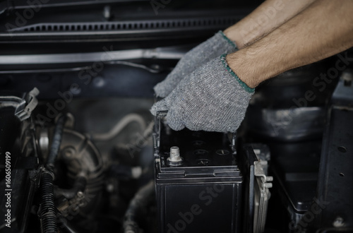Male mechanic hands pulling up car battery for replacement in engine compartment in car repair shop. Car maintenance concept.