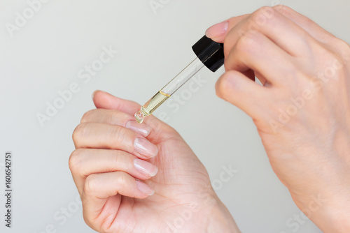 Young woman with a beautiful manicure applying a drop of oil with a pipette to the cuticle around the nails to moisturize.