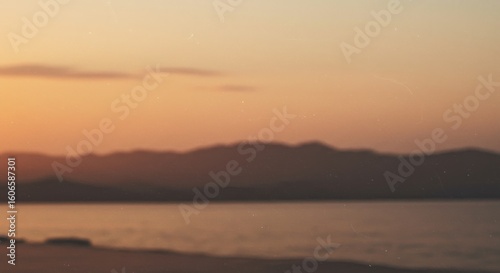 A blurry, warm sunset over a calm body of water and distant mountains.