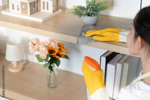 Fotografie Home Cleaning. Woman in yellow gloves dusting shelves with care.