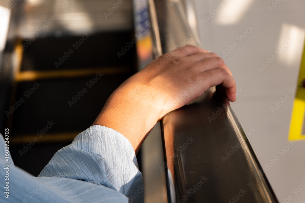Obraz premium Close-up of traveler’s hand on escalator rail. Useful for illustrating movement, safety, or detail in public infrastructure.