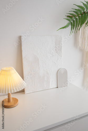 An on table lamp with a white corrugated shade and white trendy decor stand on chest of drawers. Home decor. Trendy white stylish interior.