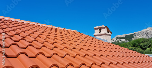 Foto A terracotta tiled roof with a stone chimney under a clear blue sky, with a moun