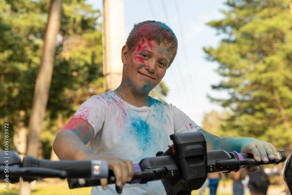 Fototapeta premium Boy covered in colorful powder riding electric scooter in park