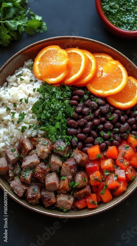 Brazilian feijoada in a clay bowl with rice, orange slices, and kale on the side.