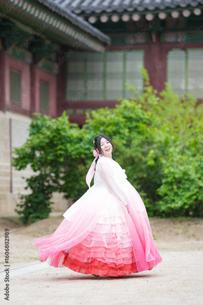 Fototapeta premium A Korean woman in her twenties wearing a charming pink hanbok twirls gracefully in front of the traditional facade of Gyeongbokgung Palace, her skirt fanning out in waves, in Seoul in June 2025.