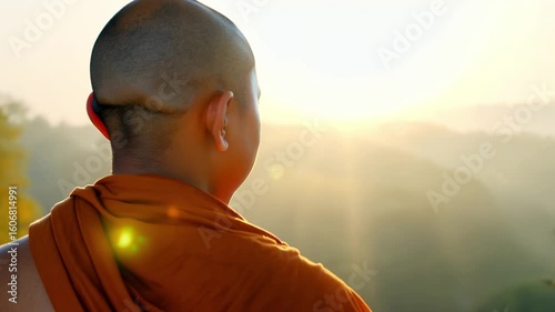 Young buddhist monk observing sunrise over misty valley