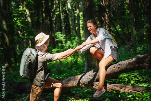 Papier peint Young male traveler helping girl to climb over fallen tree during trekking in su