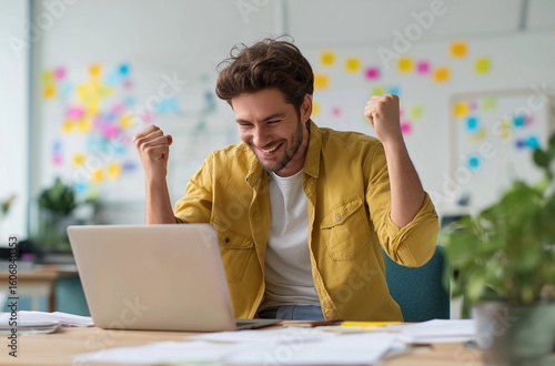 A man sits at his desk, excitedly celebrating with fists raised in front of the laptop screen displaying a website with grayscale colors and a gray background