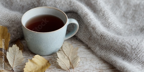 Cup of tea is sitting on a table with some leaves on it