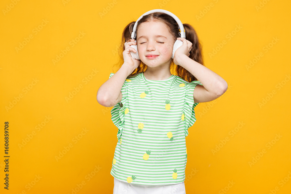 Little smiling cheery fun cute kid child girl 8-9 years old wears green t-shirt listen to music in headphones close eyes isolated on plain yellow background Mother's Day love family lifestyle concept Little smiling cheery fun cute kid child girl 8-9 years old wears green t-shirt listen to music in headphones close eyes isolated on plain yellow background Mother's Day love family lifestyle concept