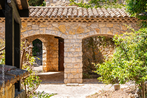 Rustic stone archway in Mediterranean garden, traditional Provencal architecture in sunlight