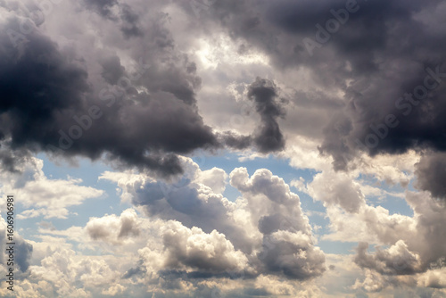 Dark clouds above and light clouds below intersect in the sky, dark and white swirling clouds divide the sky in half close-up, weather change as a sign of bad weather