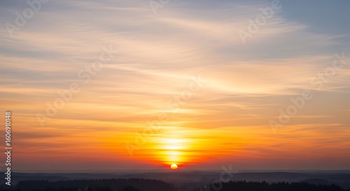 A vibrant sunset with orange and yellow hues painting the sky above a dark silhouetted landscape