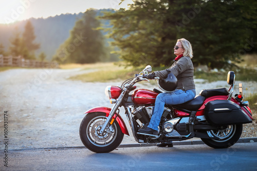 Murais de parede Stylish mature woman on a red cruiser motorcycle, enjoying a peaceful moment at sunset in nature
