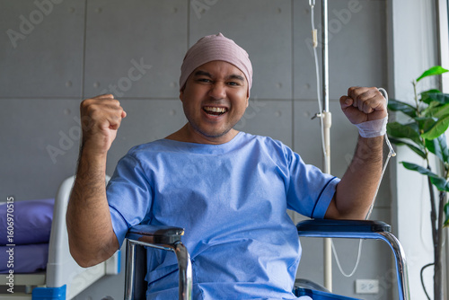 Asian man cancer patient smiling and happy with health checkup result after listening to oncologist explanation while sitting on wheelchair  in hospital ward.