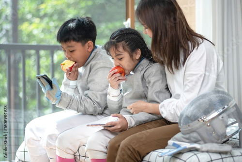 The fencer relaxes by spending time on his cell phone and eating an apple while his mother looks after them. Caring for growing children