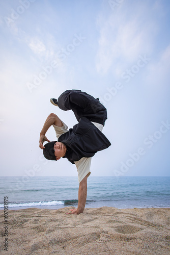 砂浜で片手倒立を決めるブレイクダンサー