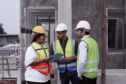 Fotografie Group of engineers and supervisors discussing blueprint at prefab concrete panel factory, wearing safety vests and helmets, planning next production phase on site