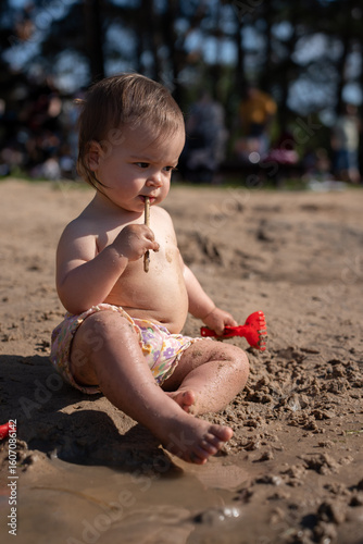 Photos curious toddler seated on sandy beach amidst sunlight, exploring stick and holdi