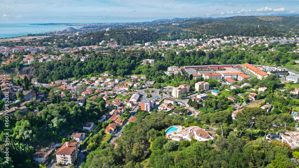 Fototapeta premium Aerial view of a vibrant residential area surrounded by lush greenery and hills, showcasing a mix of modern and traditional architecture with a distant coastline