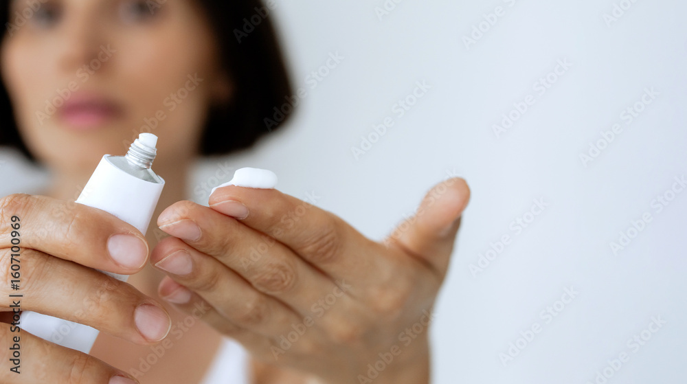 Naklejka premium Woman Applying ointment from White Tube on Finger – Skincare, Treatment, Dermatology, Close-Up of Hands with Soft Focus Face in Background
