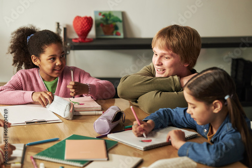 Papier peint Caucasian teenage boy interacting with Black girl and Caucasian girl while sitti