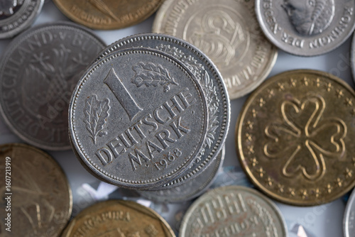 Close up of one deutsche mark on top of stack, uncirculated coin from West Germany with dents and scratches, other coins are blurred in background