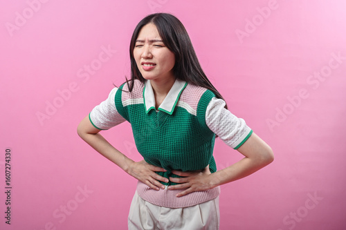 Canvas Print Asian woman clutching her stomach with a pained facial expression, suggesting ab