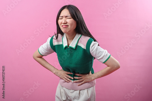 Photography Asian woman clutching her stomach with a pained facial expression, suggesting ab