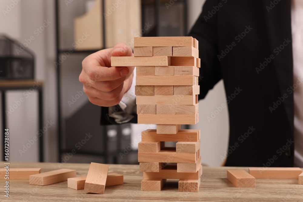 Lviv, Ukraine - December 08, 2023: Playing Jenga. Man removing wooden block from tower at table indoors, closeup Lviv, Ukraine - December 08, 2023: Playing Jenga. Man removing wooden block from tower at table indoors, closeup