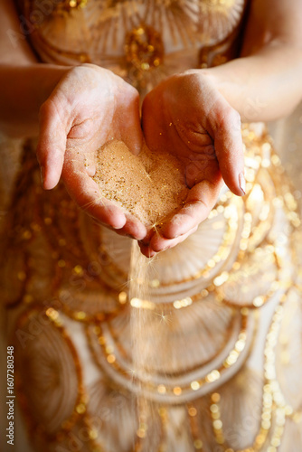 New York City, NY  USA. Golden sand slipping between the fingers of a woman's hands. 