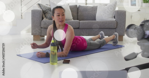 Korean instructor holding plank on yoga mat in living room, with camera, water bottle, smartphone