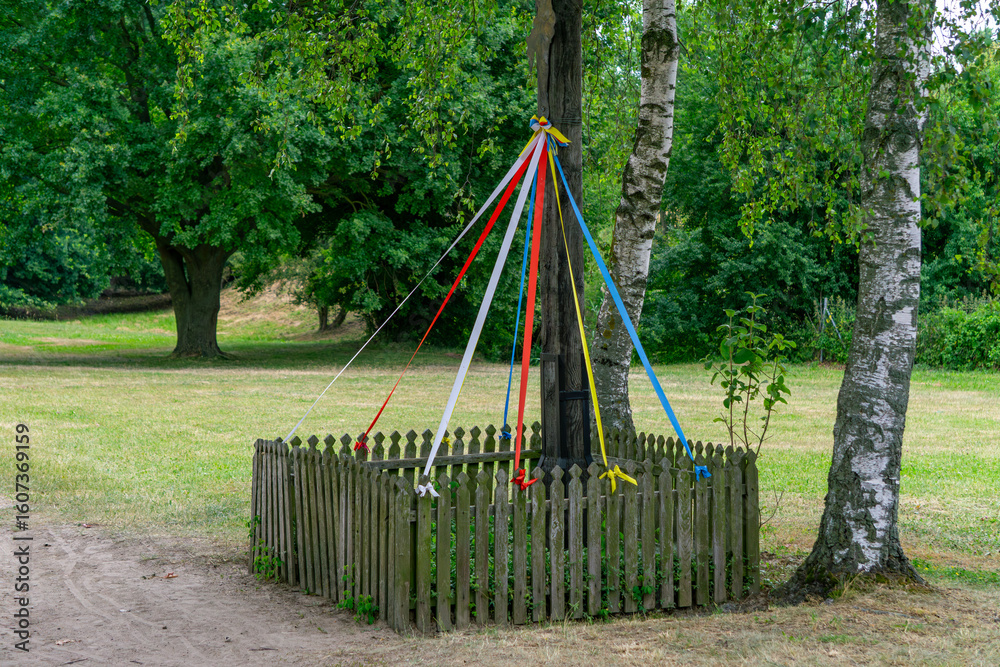 Traditional maypole with colorful ribbons, surrounded by a wooden fence in a green park. Folk decoration in a natural outdoor setting. Traditional maypole with colorful ribbons, surrounded by a wooden fence in a green park. Folk decoration in a natural outdoor setting.
