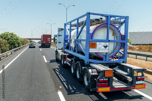 Truck with a tank container carrying titanium tetrachloride, marked with toxic and corrosive hazard placards and an 'X' indicating water-reactive substance.