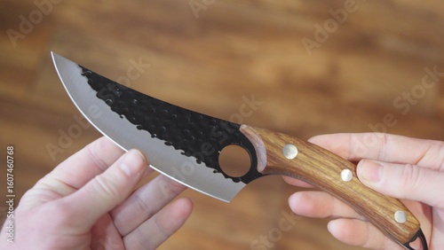 Close-up of hands holding a hammered kitchen knife with a hole in the blade and a wooden handle