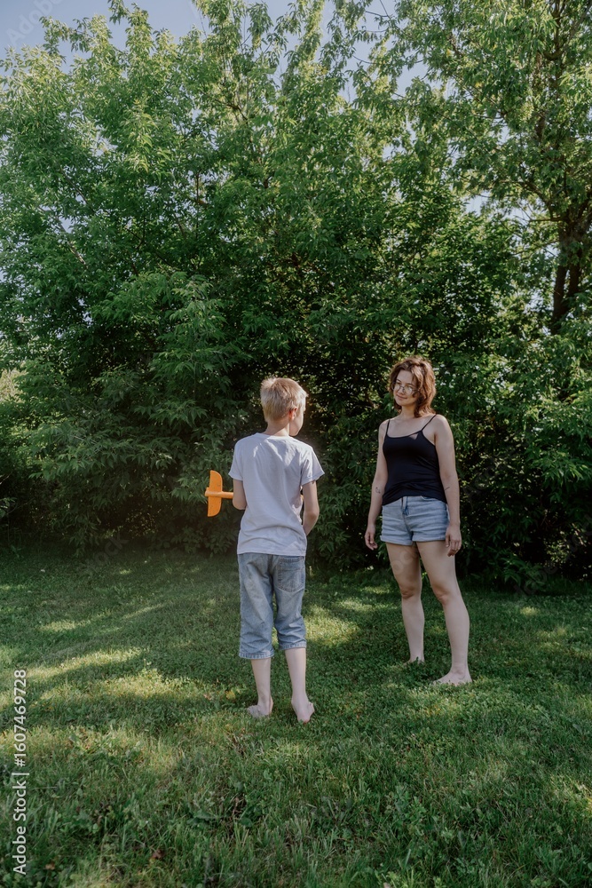 A mother and her son with hearing aids joyfully launch a paper airplane in a sunlit park, capturing a heartwarming moment of inclusive play and bonding in nature A mother and her son with hearing aids joyfully launch a paper airplane in a sunlit park, capturing a heartwarming moment of inclusive play and bonding in nature