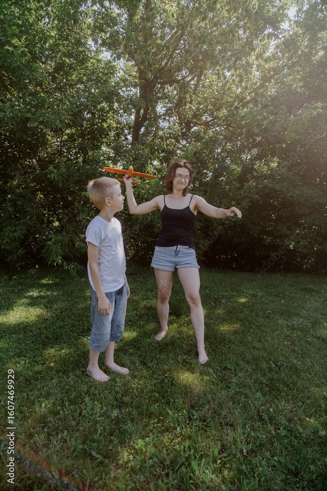 Fototapeta premium A mother and her son with hearing aids launch a paper airplane in a park, a heartwarming moment of inclusive play and bonding in nature. Perfect for disability awareness and family lifestyle content