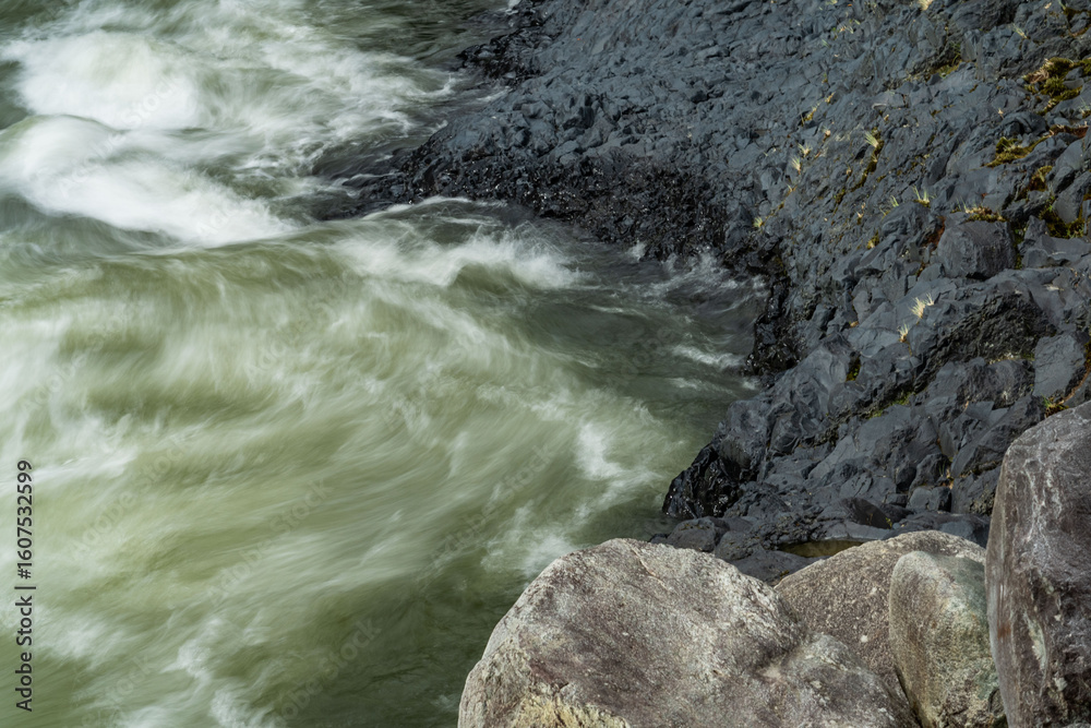 Naklejka premium textures of the power of water between black volcanic rocks in a river that is turquoise and green in color
