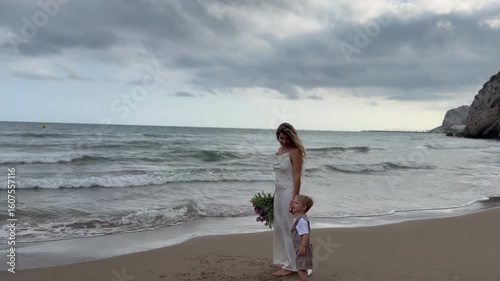 Mother and child standing on sandy beach with bouquet

